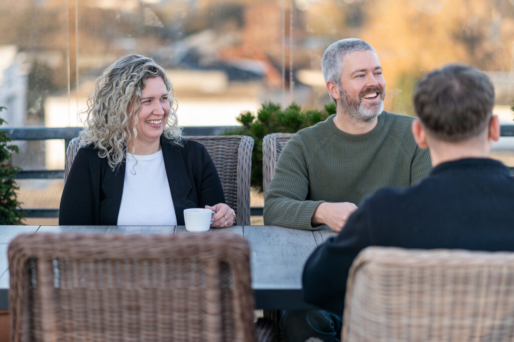 Zwei Mitarbeitende von RBM Ritzmann + Dr. Blödorn sitzen auf der Dachterrasse und sprechen mit einem Mandanten, der mit dem Rücken zur Kamera sitzt – persönliche Beratung in Steuerberatung und Wirtschaftsprüfung.