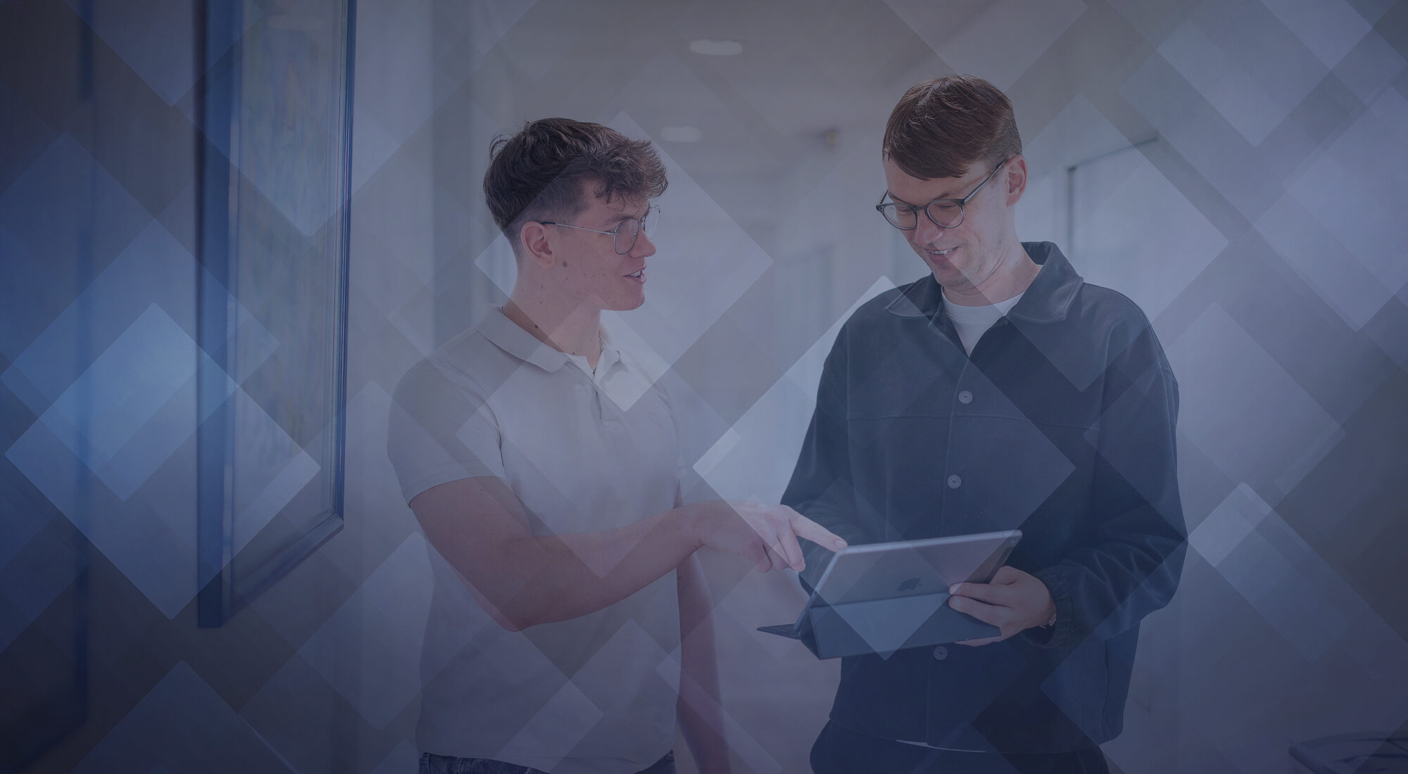 Ein Partner von RBM Ritzmann + Dr. Blödorn (rechts) im Gespräch mit einem Kollegen im Büro; der Partner lächelt und blickt nach unten – Zusammenarbeit in Steuerberatung und Wirtschaftsprüfung.